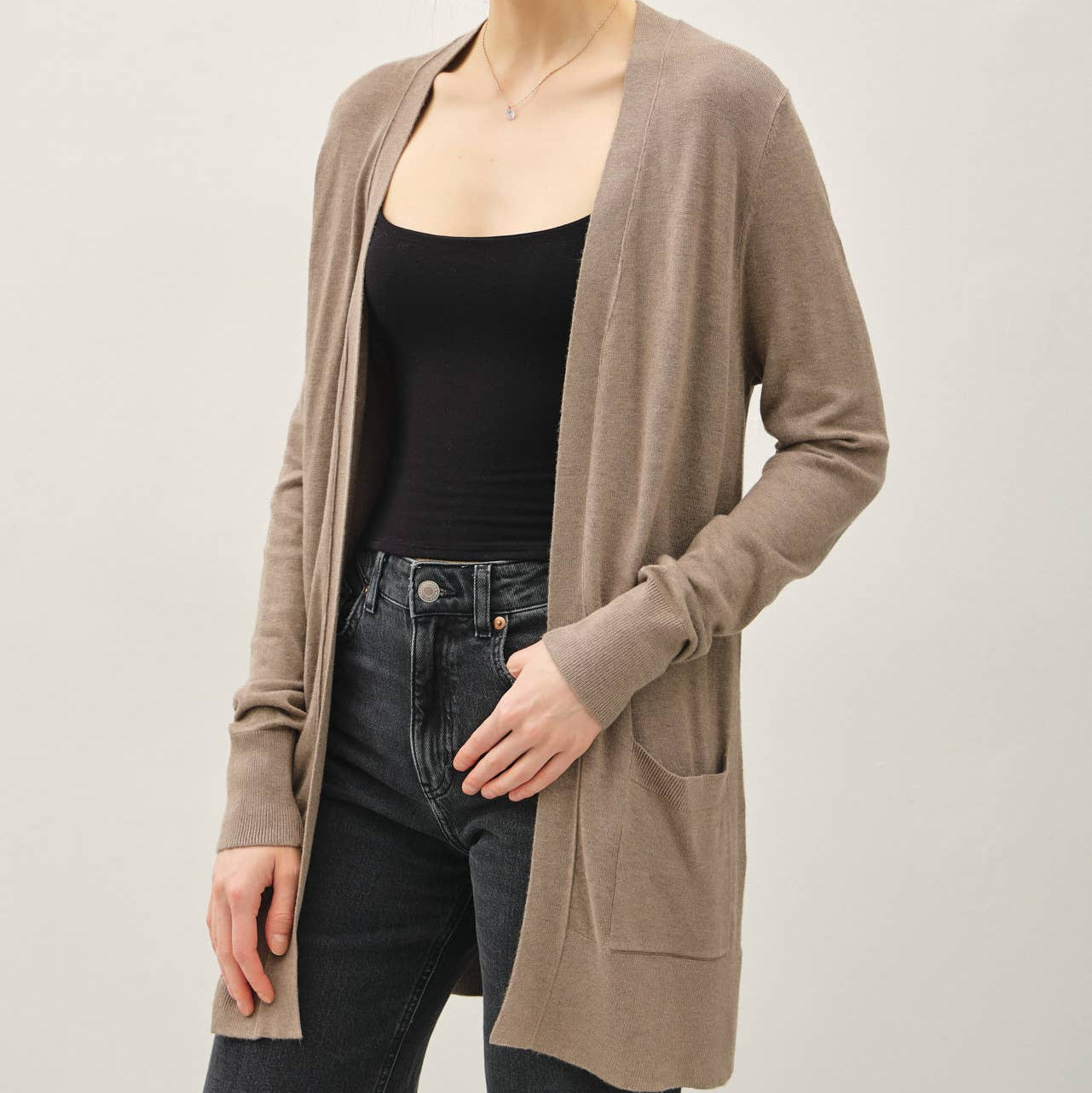 Woman wearing a beige cardigan over a black top and jeans on a plain background