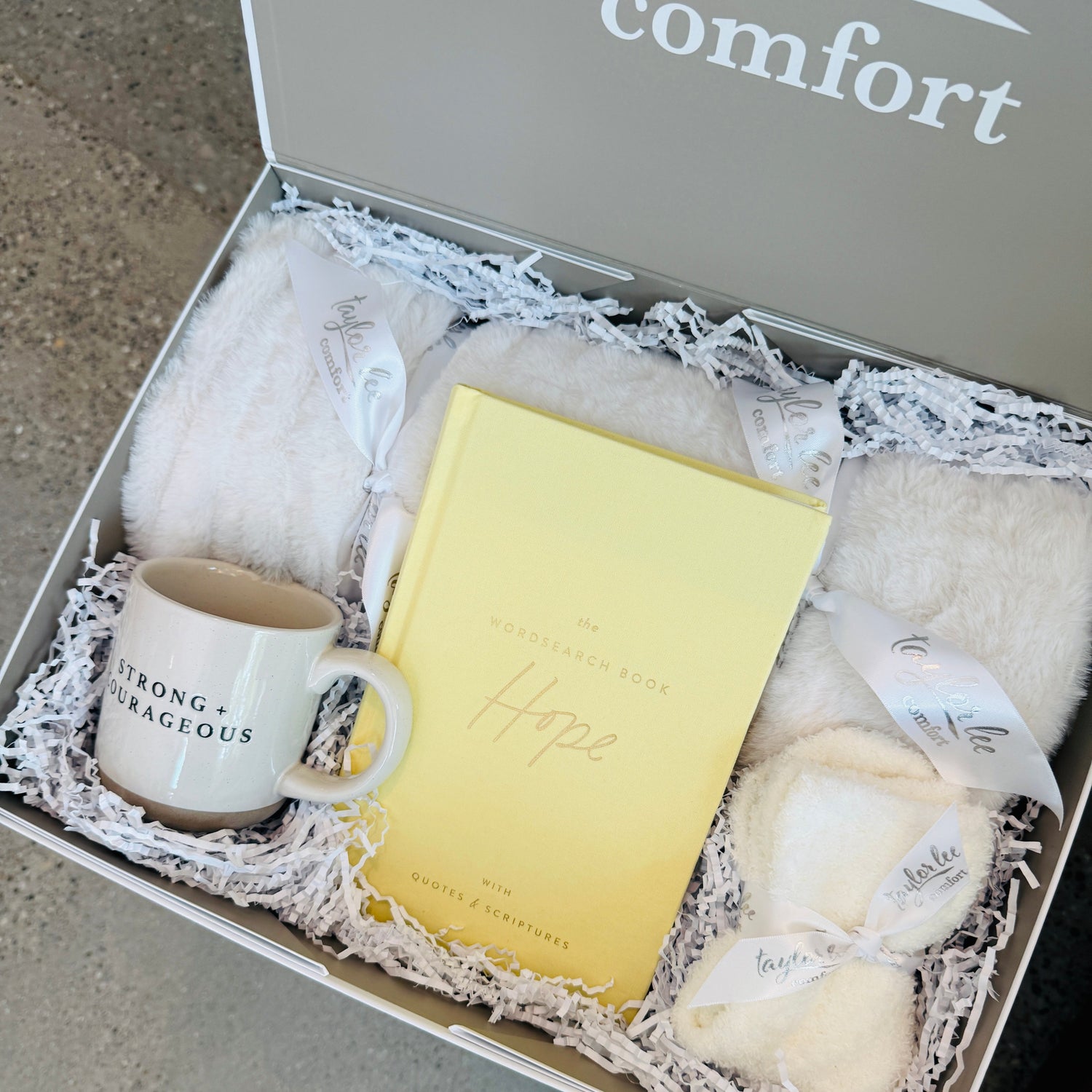 Soft and Cozy Cream Colored blanket and ceramic mug that says strong + courageous. Quotes and Scripture Wordsearch interactive book that says is focused on hope. Paired with a cozy pair of one size fits all socks