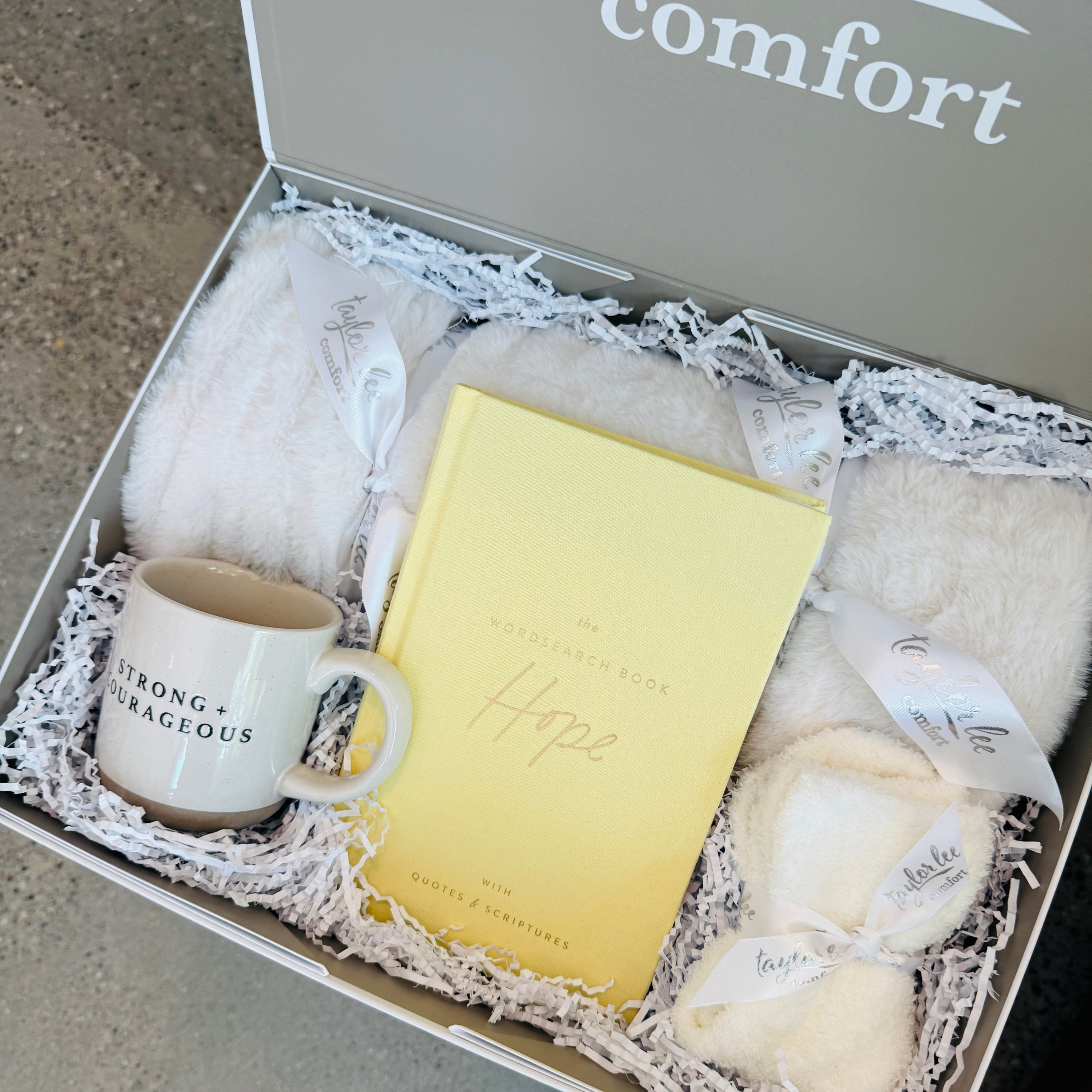 Soft and Cozy Cream Colored blanket and ceramic mug that says strong + courageous. Quotes and Scripture Wordsearch interactive book that says is focused on hope. Paired with a cozy pair of one size fits all socks