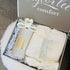 An open gift box from Taylor Lee Comfort containing a cream-colored robe with a lace detail, a wine glass labeled &