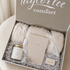 Taylor Lee Comfort wedding or anniversary gift set in an open gift box, featuring cream colored plush blanket, a candle jar, and cream colored journal that says "vows" on the front and safety matches that say "the perfect match" nestled in shredded paper, with the brand name printed on the inside lid.