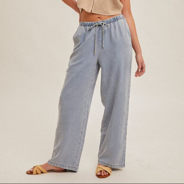 Woman wearing a beige sleeveless top and light blue pants on a plain background