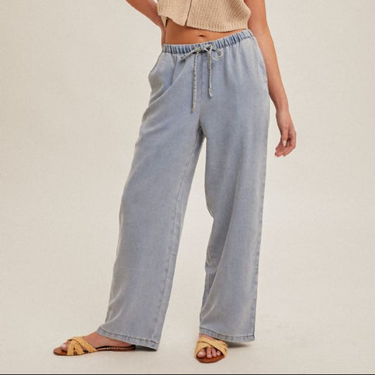 Woman wearing a beige sleeveless top and light blue pants on a plain background