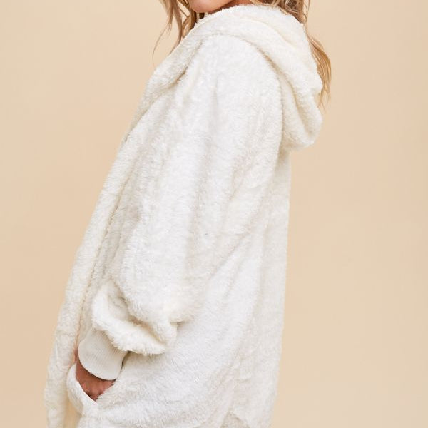 Woman wearing a white fluffy cardigan, blue jeans, and a brown hat against a beige background